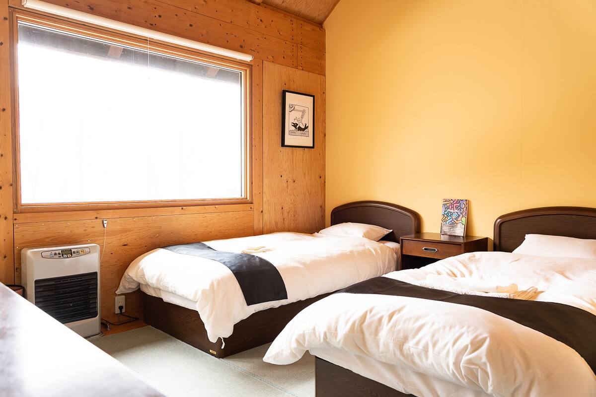 A room with two beds, a window, a heater, and a framed picture on the wall.