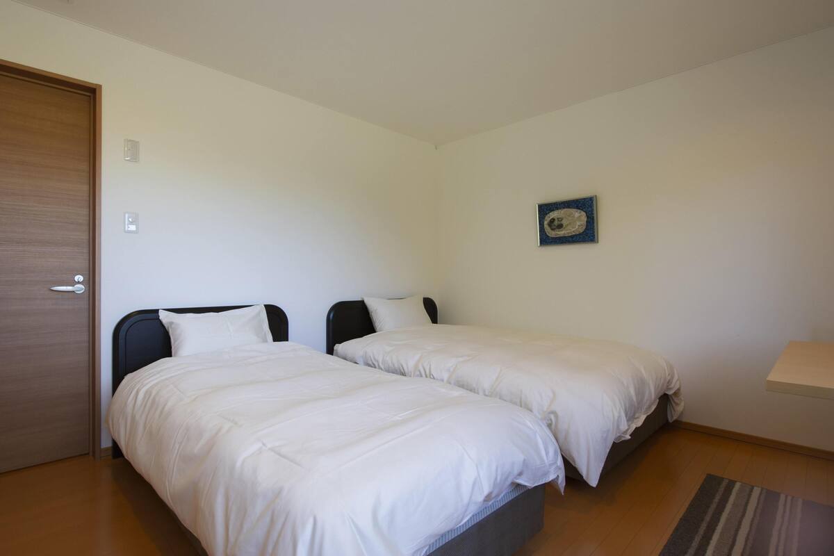 A bedroom with two beds, a door, a small wall-mounted picture, and a bedside table.