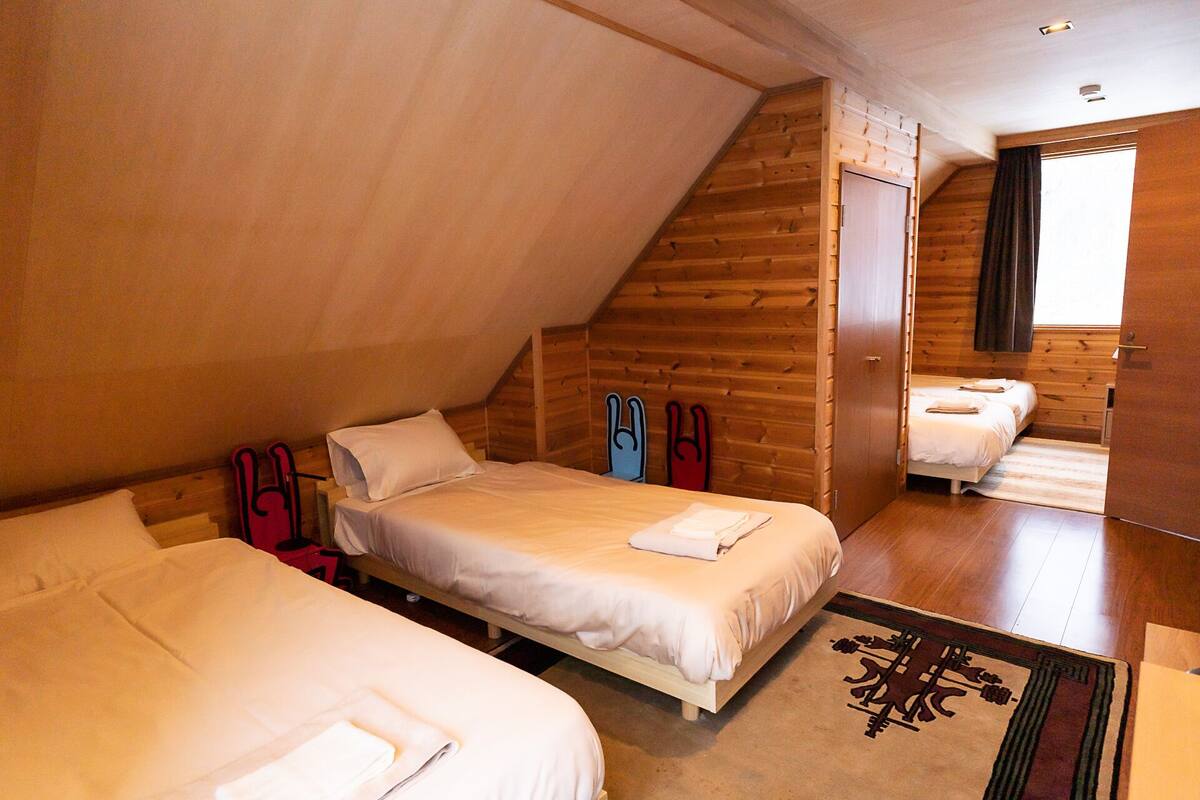 A cozy attic bedroom with two beds, wooden walls, and a large window.