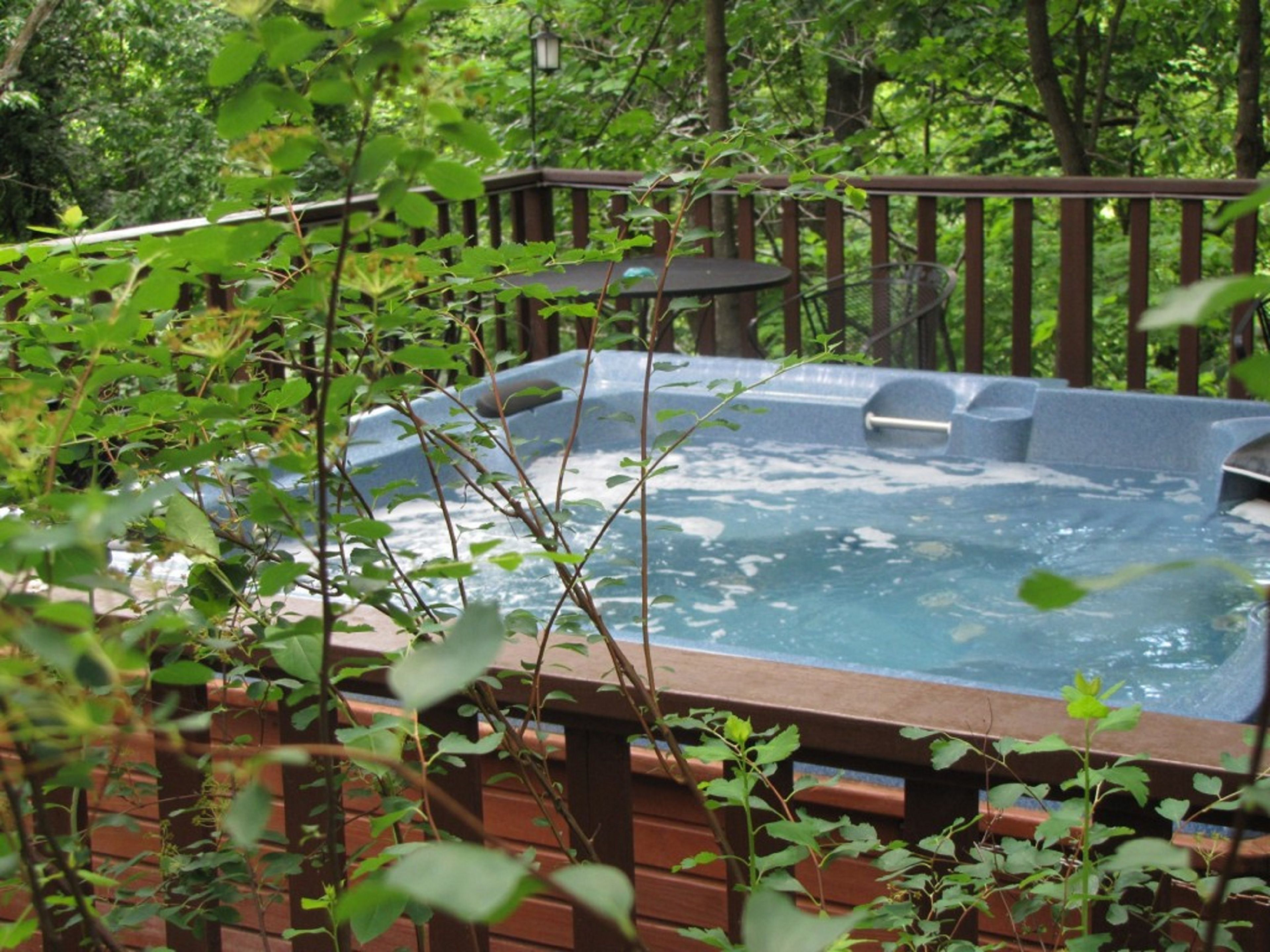 A hot tub surrounded by a wooden deck and lush greenery.
