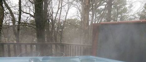 A hot tub with a wooden deck and a view of trees in the background.