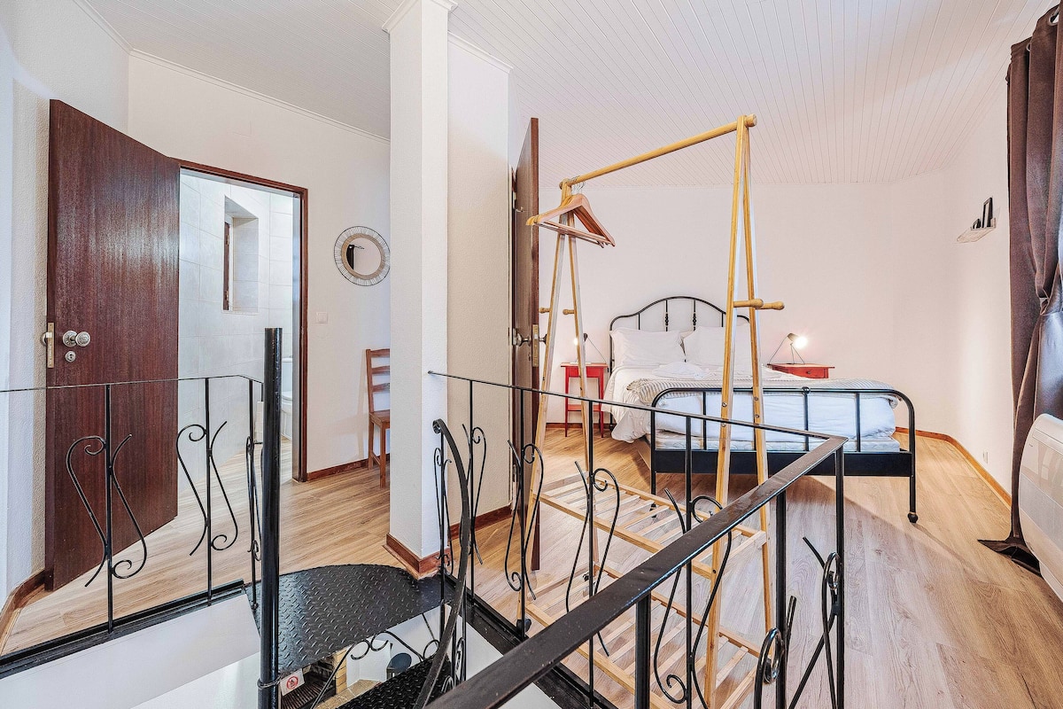 A bedroom with a bed, a wooden ladder, a hanging chair, and a small table.