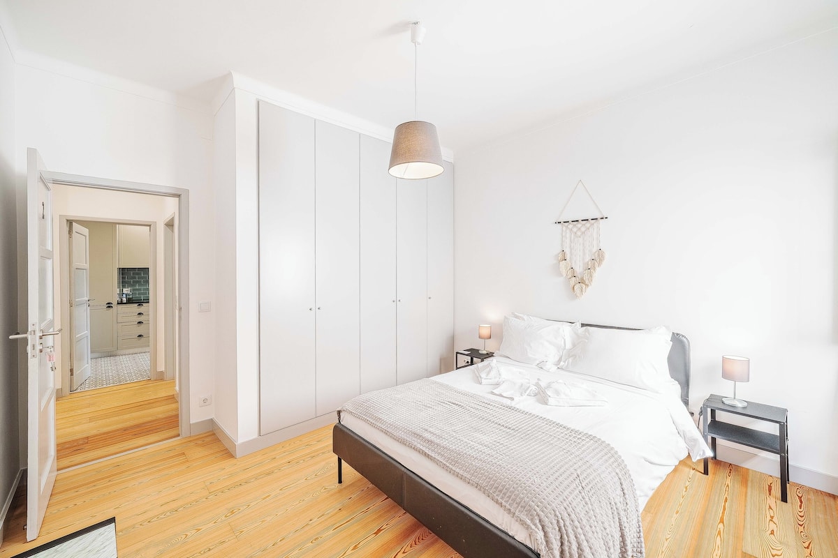 A bedroom with a bed, bedside tables, a hanging light fixture, and a wardrobe.
