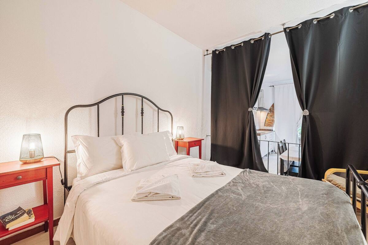 A neatly made bed with white linens, a bedside lamp, and a nightstand with a book.