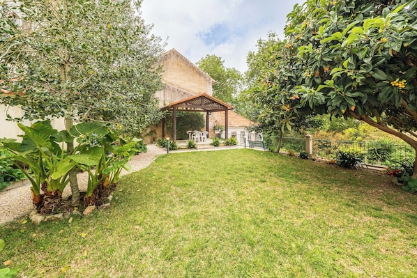 A garden with a gazebo, a lawn, and a building with a sloped roof.