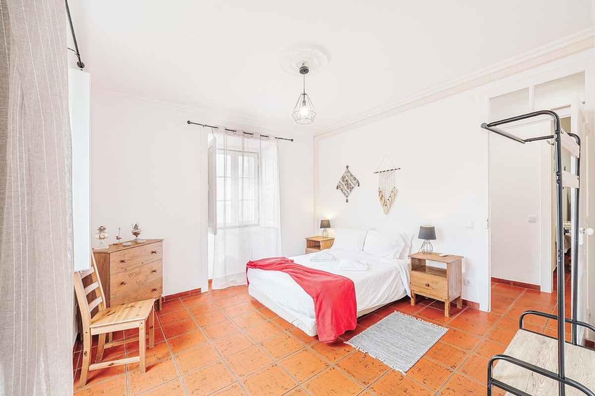 A bedroom with a bed, wooden dresser, bedside tables, and a chair.