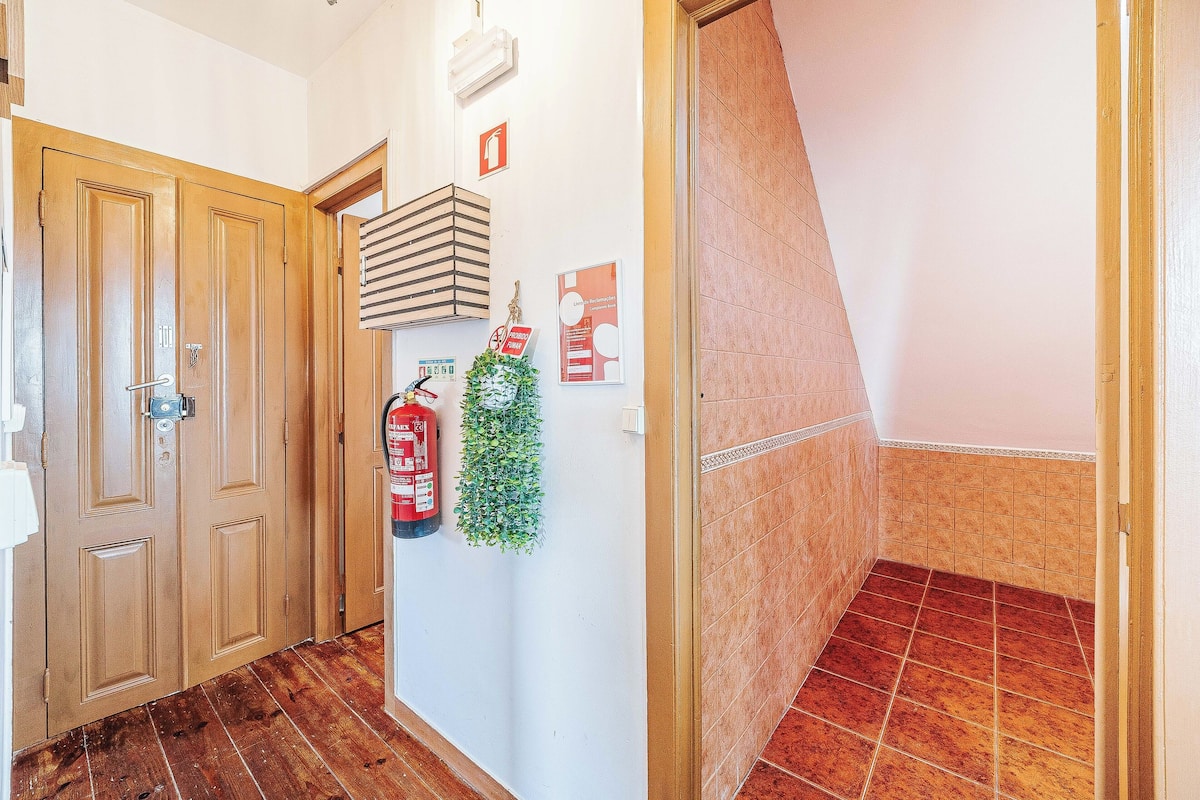 A hallway with wooden doors, a fire extinguisher, a small plant, and a tiled floor.