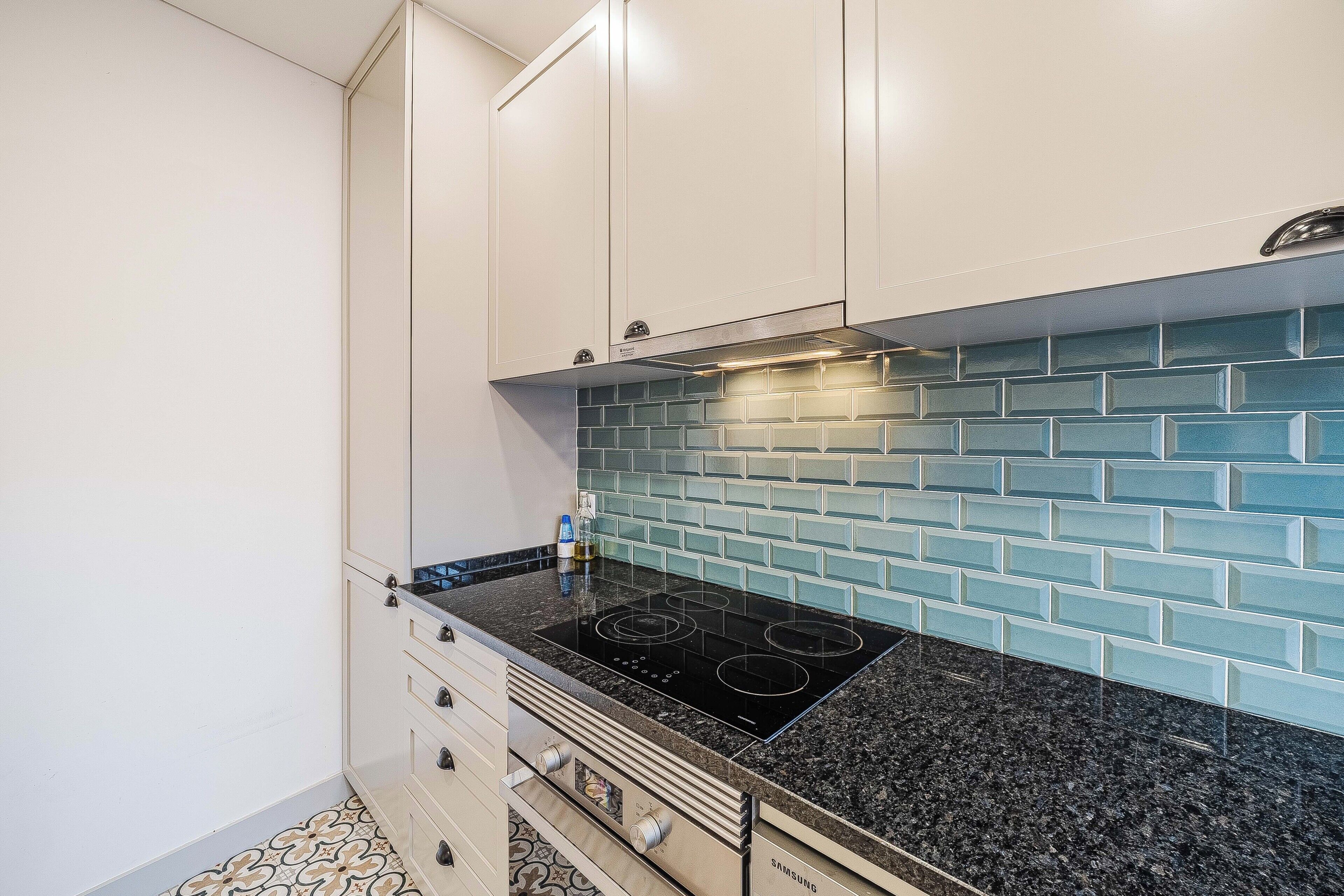 A kitchen with white cabinets, a black countertop, and a blue-tiled backsplash.