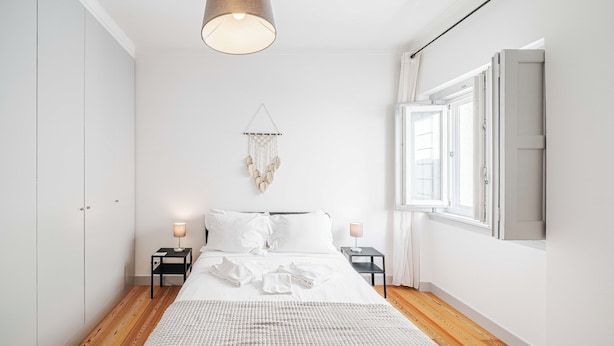 Un dormitorio con cama, mesitas de noche, una decoración de macramé colgante y una ventana con cortinas.