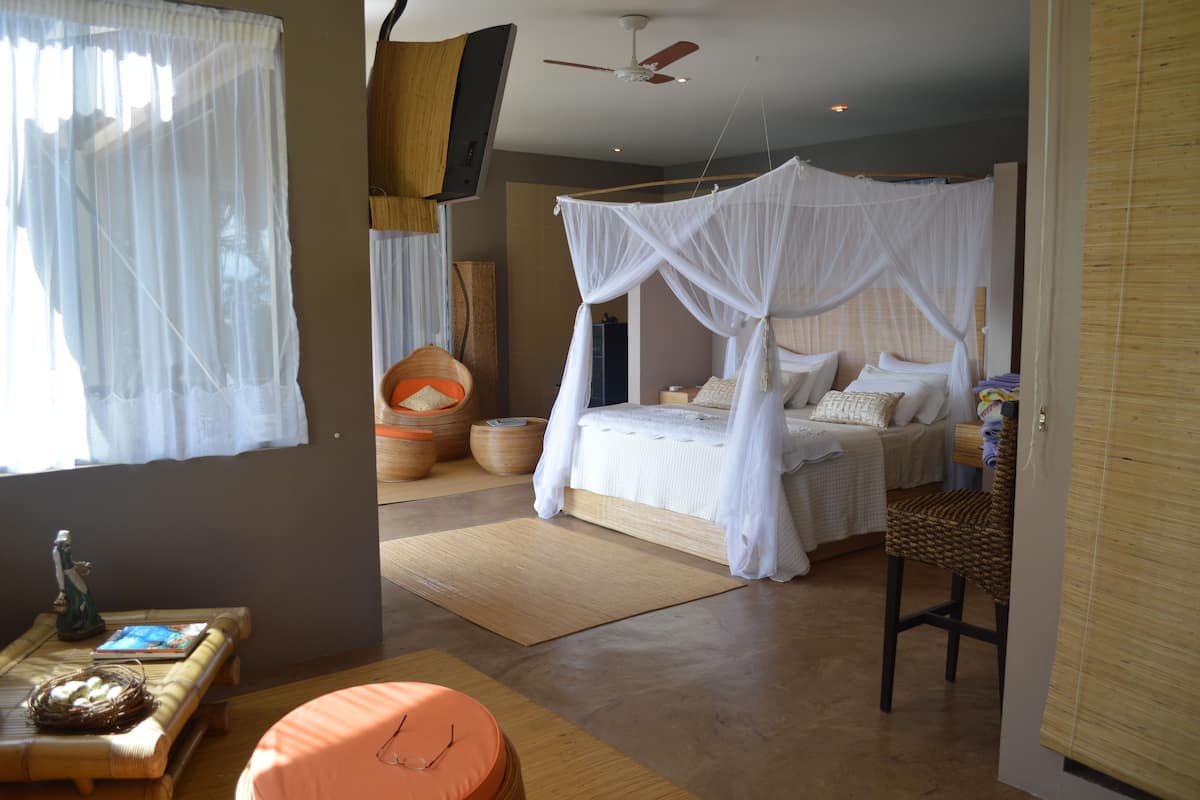 A bedroom with a canopy bed, a television mounted on the wall, and a wooden floor.