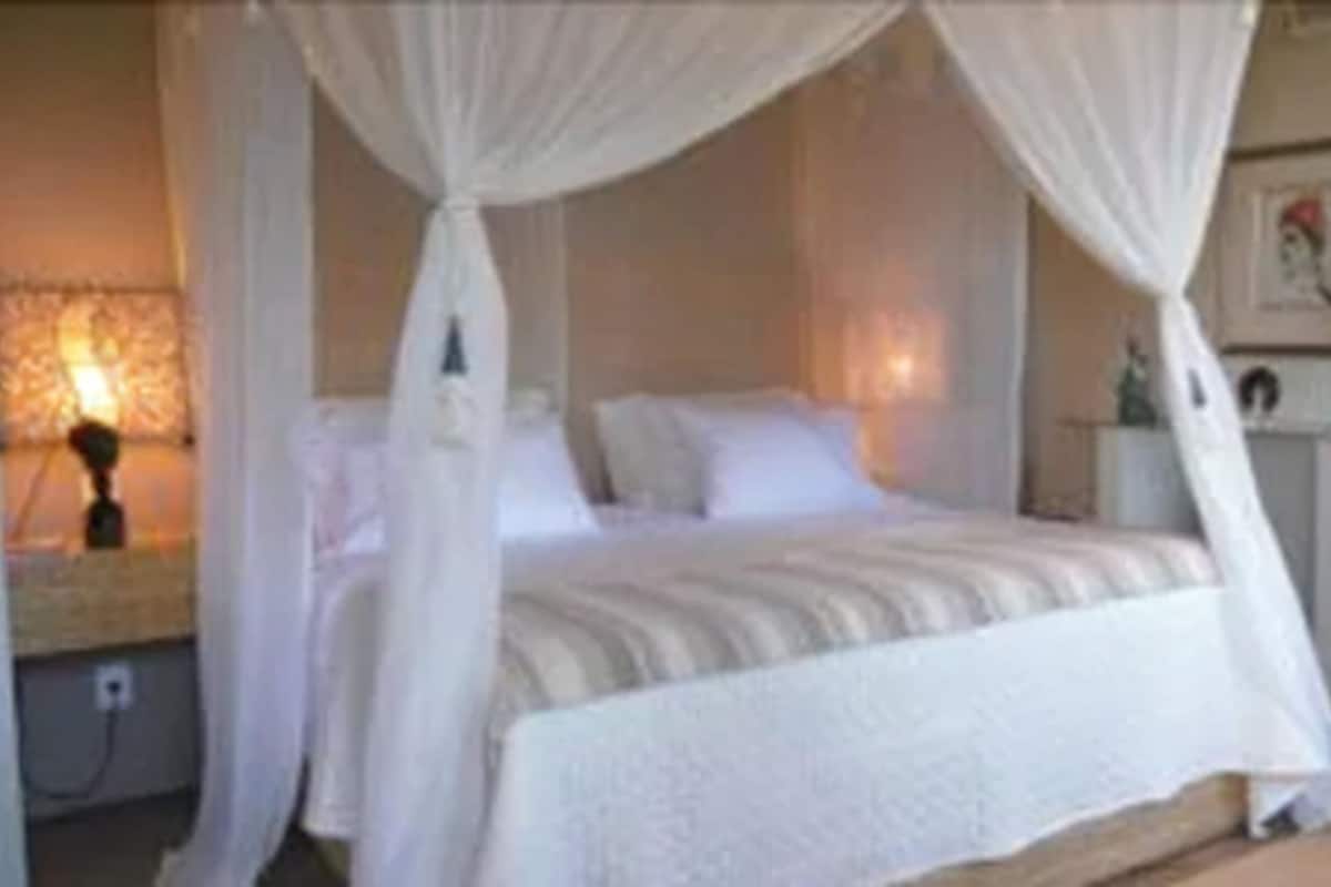A bedroom with a canopy bed, a bedside table, a chair, and a wall-mounted lamp.
