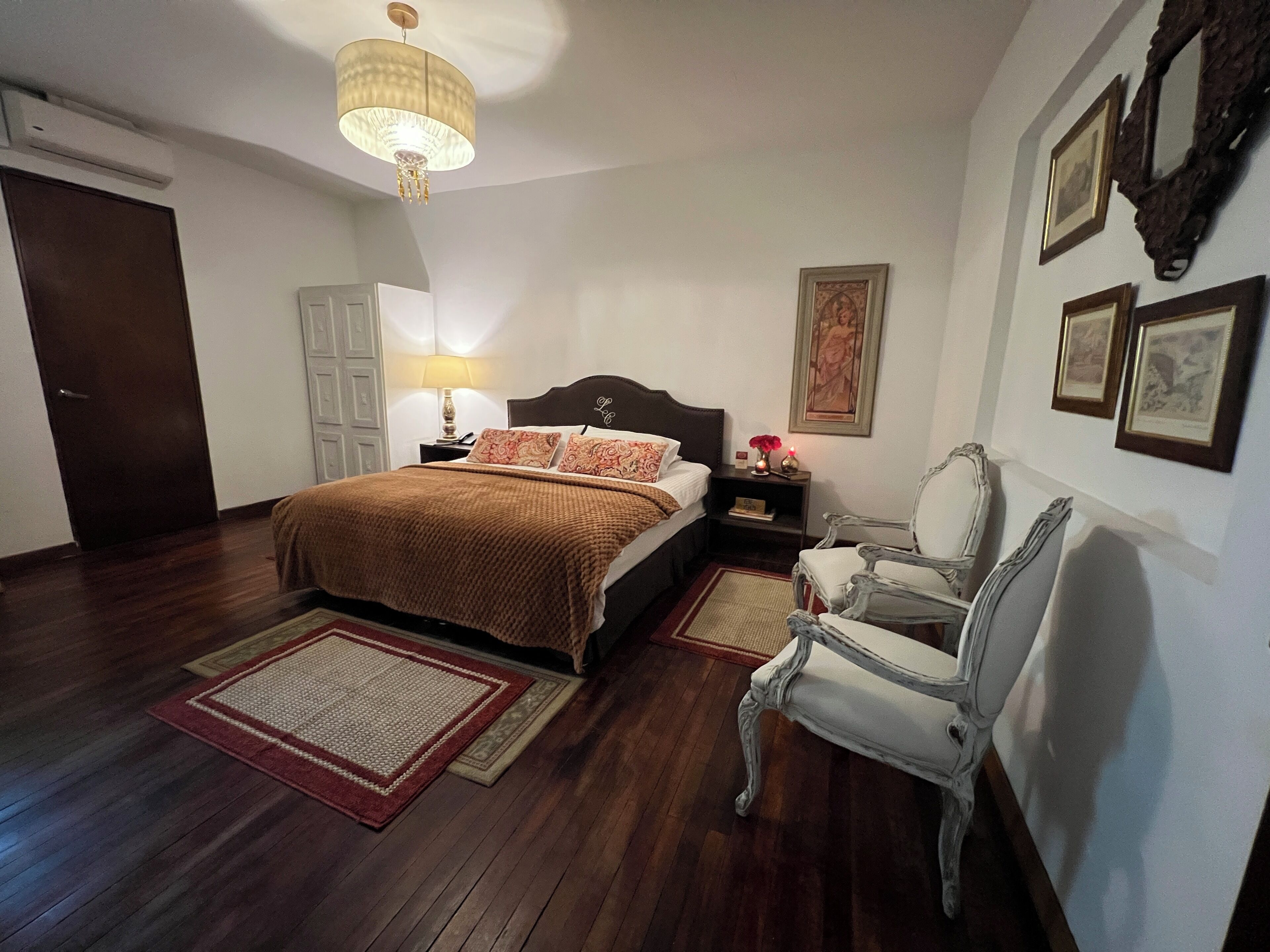 A bedroom with a bed, nightstand, lamp, chair, and wall-mounted artwork.