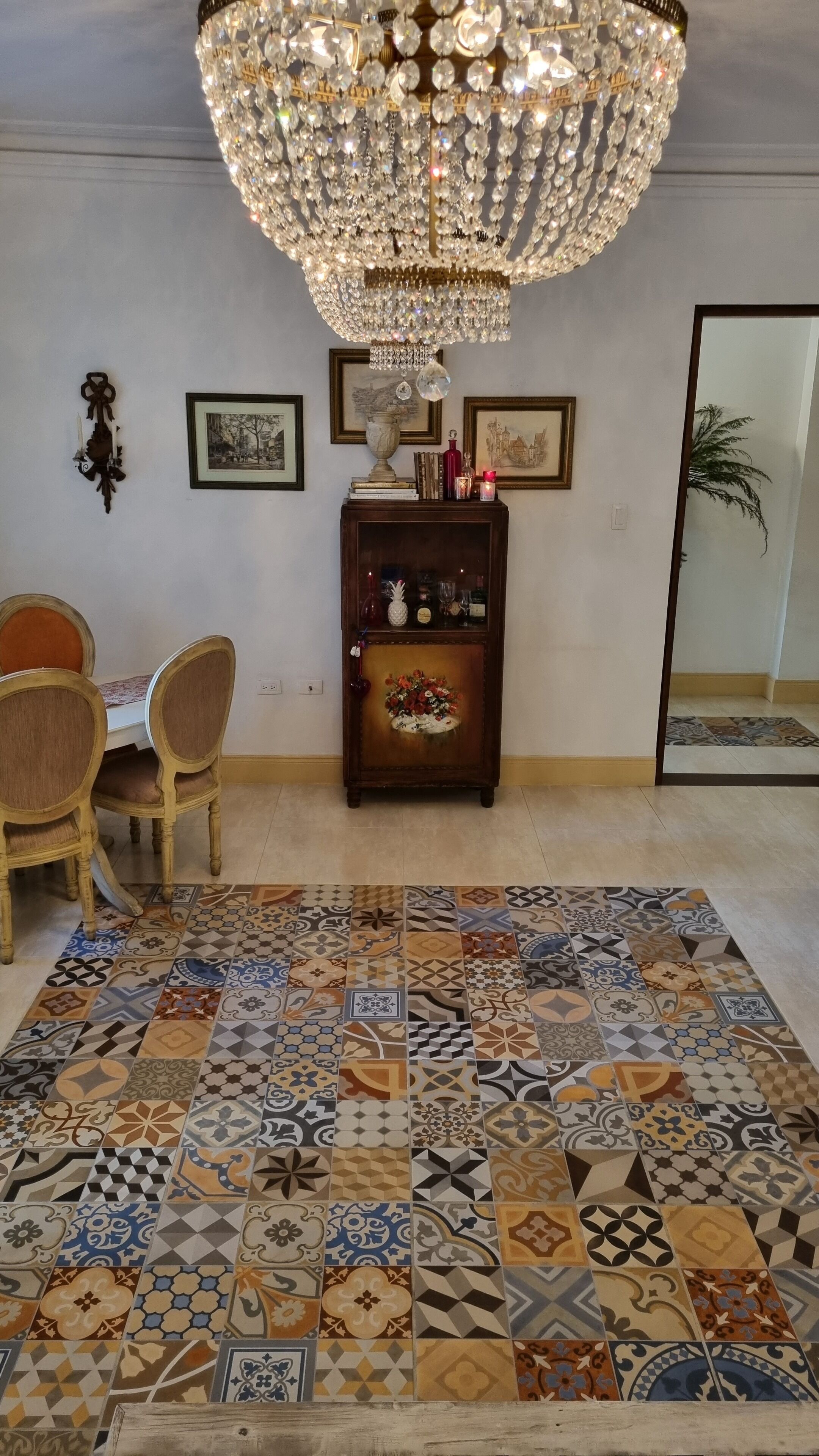 Ein Essbereich mit einer Chandelier, gerahmten Bildern, einem Holzservenmöbel und einem gemusterten Teppich.