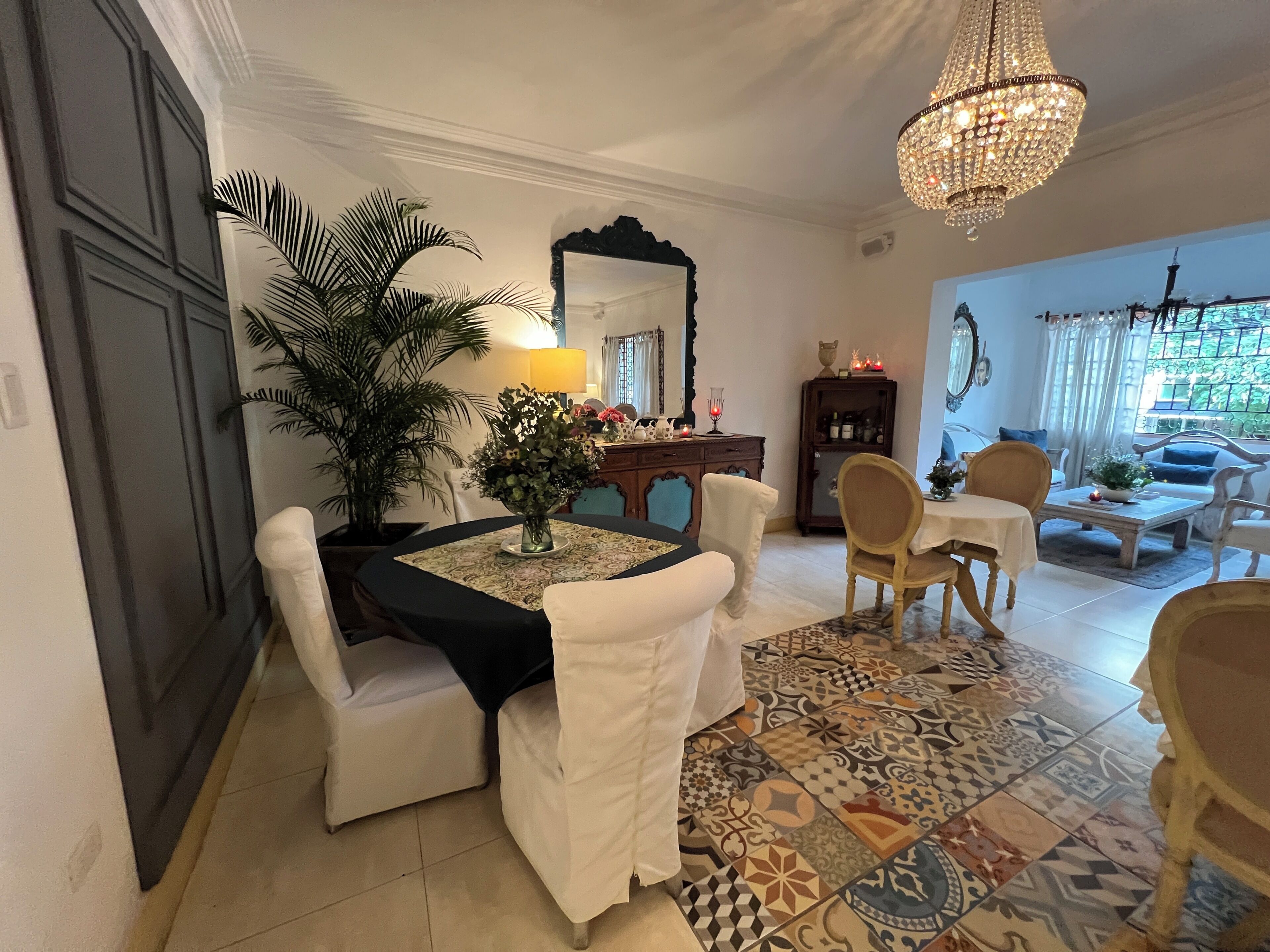 A dining area with a table, chairs, a chandelier, a potted plant, and a mirror.