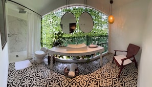 A bathroom with a curved sink, two mirrors, a hanging light fixture, a patterned floor, and a chair. - Leclerc Hotel Boutique Granada (Cali)
