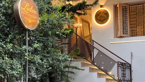 Een hotelingang met een bord, een trap met een leuning en een wandlamp.