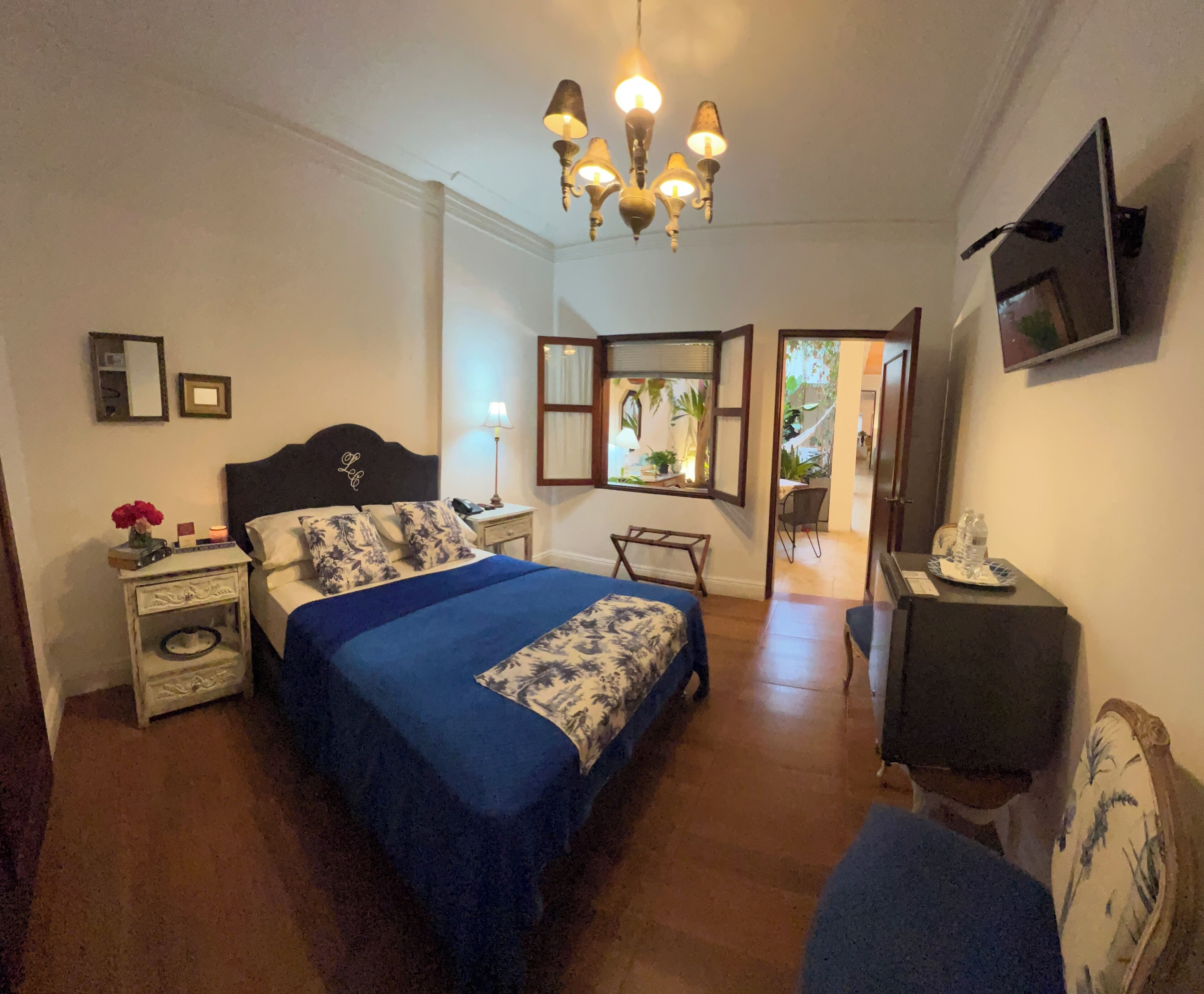 Un dormitorio con cama, mesita de noche, lámpara, televisor y vistas al exterior.