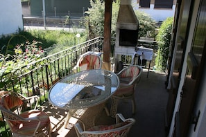 A balcony with wicker furniture, a glass table, and a wood-burning stove. - Alojamientos Acá y Allá - Hostel (Esteribar)