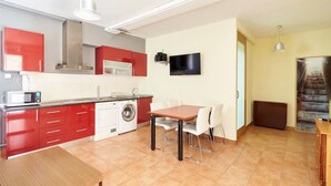 A compact kitchen with red cabinets, a microwave, a washing machine, and a dining area with a table and chairs. - Alojamientos Acá y Allá - Hostel (Esteribar)