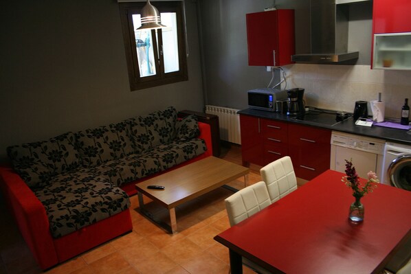 Espaço compacto para viver, com sofá, pequena mesa de jantar, máquina de café e máquina de lavar.
