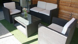 A wicker sofa set with cushions, a glass coffee table, and a vase with flowers. - Alojamientos Acá y Allá - Hostel (Esteribar)