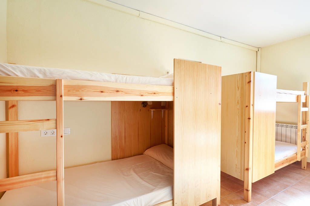 A room with three bunk beds made of wood, a white wall, and a tiled floor.
