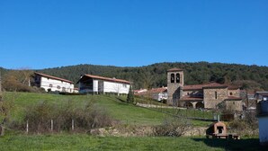 A rural setting with a stone church, a white building with a red roof, and a green hillside. - Alojamientos Acá y Allá - Hostel (Esteribar)