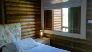Ein Zimmer in einer Holzhütte mit einem Bett, einem Nachttisch, einer Lampe und einem Fenster mit Fensterläden.