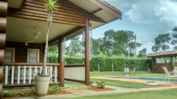 Eine Holzhütte mit überdachter Veranda, einem kleinen Garten und einem Poolbereich.