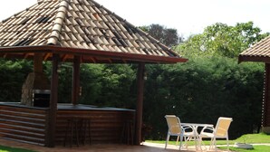 Ein hölzerner Pavillon mit Ziegeldach, ein Grillplatz und eine Sitzgruppe am Pool.