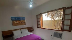 A bedroom with a bed, a ceiling fan, a window with a view of trees, and a painting on the wall. - Pousada Água da Fonte (Florianópolis)