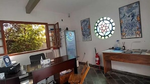A modern kitchen with a dining area, featuring a wooden table, chairs, a refrigerator, and decorative wall art. - Pousada Água da Fonte (Florianópolis)