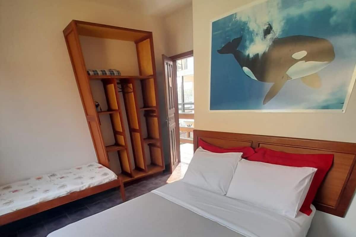 A bedroom with a bed, a wooden wardrobe, a bench, and a painting of a whale.