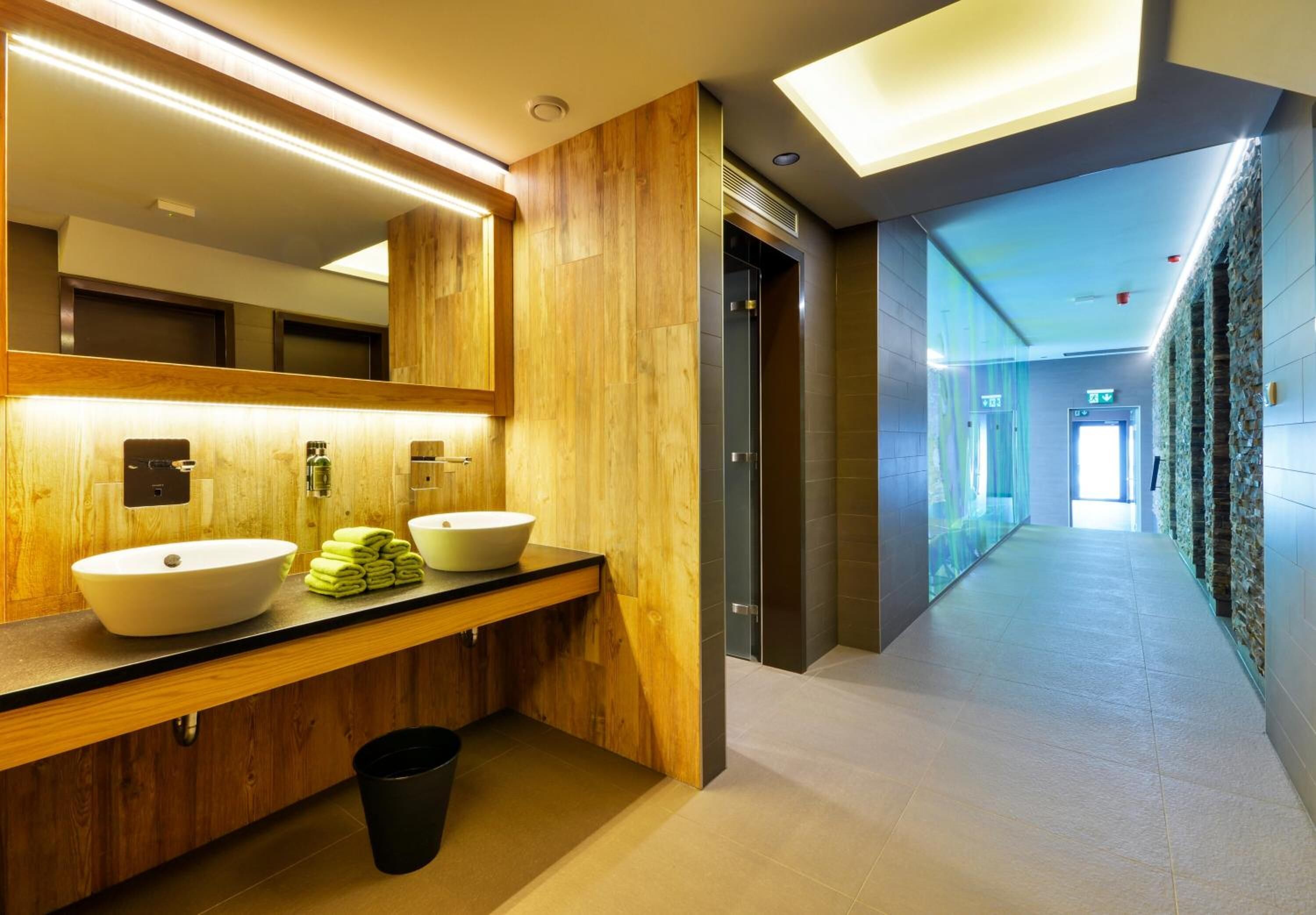 Een moderne badkamer met houten details, twee wastafels en een grote spiegel.