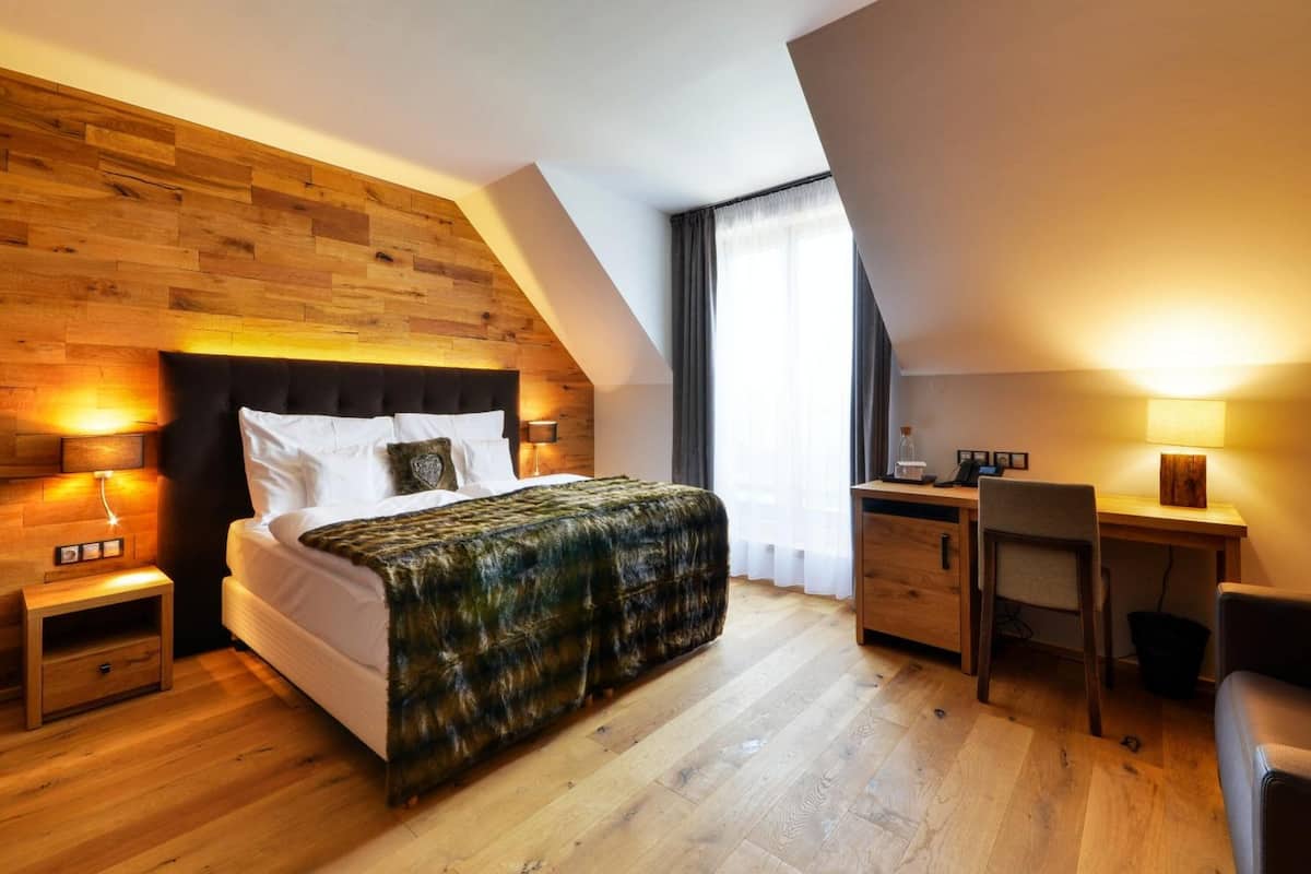 Un dormitorio moderno con cabecera de madera, una cama grande con manta estampada, un escritorio y una silla.