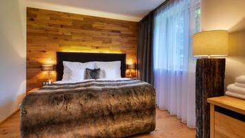 Un dormitorio moderno con cabecera de madera, una colcha mullida y grande, dos lámparas de noche y vistas a un bosque a través de cortinas traslúcidas.