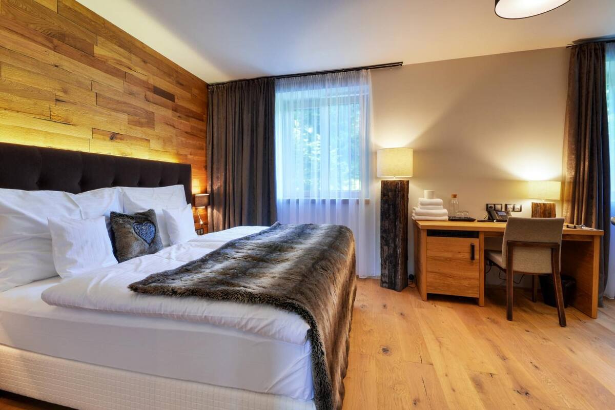 Habitación de hotel con una cama grande, cabecera de madera, escritorio con silla y ventana con cortinas.