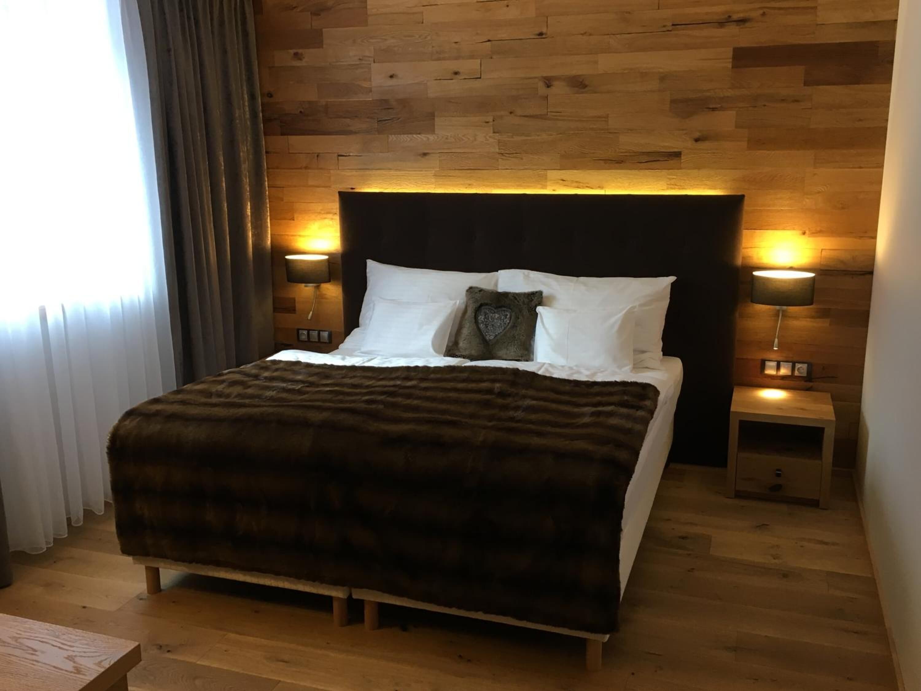 A neatly made bed with a dark brown cover, two bedside lamps, and a wooden headboard.