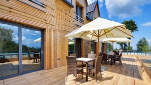 Un patio al aire libre con suelo de madera, mobiliario de mimbre y una sombrilla grande.