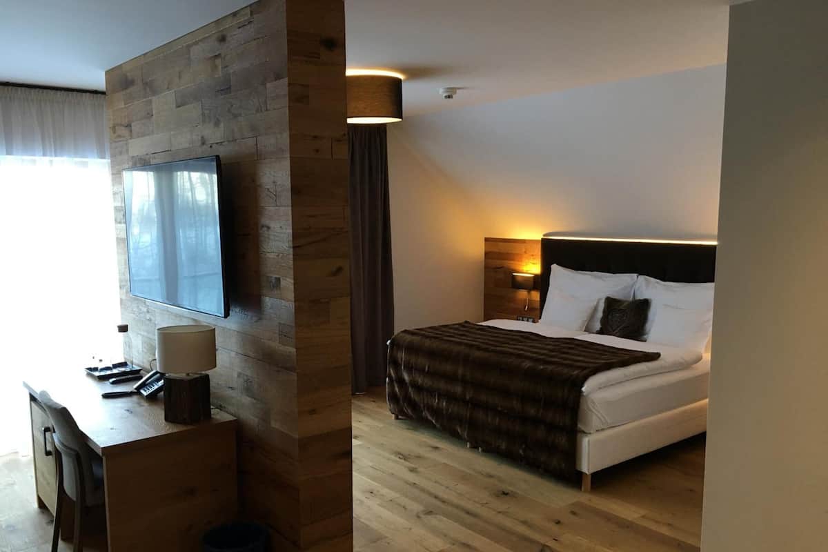 Habitación de hotel con un escritorio de madera, una cama con cabecero, un televisor montado en la pared y una lámpara.