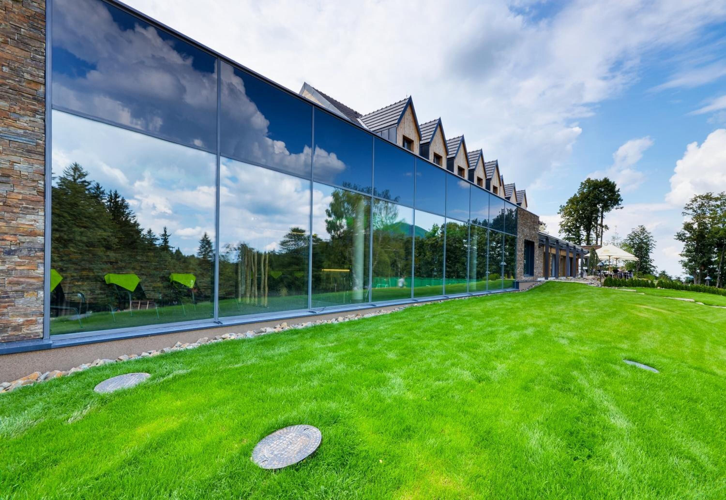 A modern building with large glass windows reflecting the sky and trees.