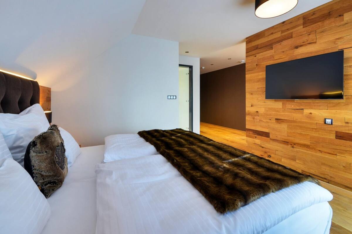 Una habitación de hotel moderna con una cama grande, un muro decorativo de madera, un televisor de pantalla plana montado en la pared y una puerta que da a otra habitación.