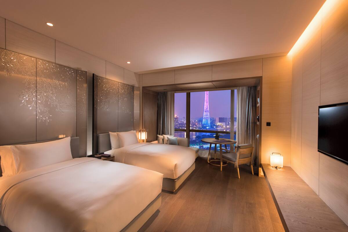 A modern hotel room with two beds, a small table, and a TV.