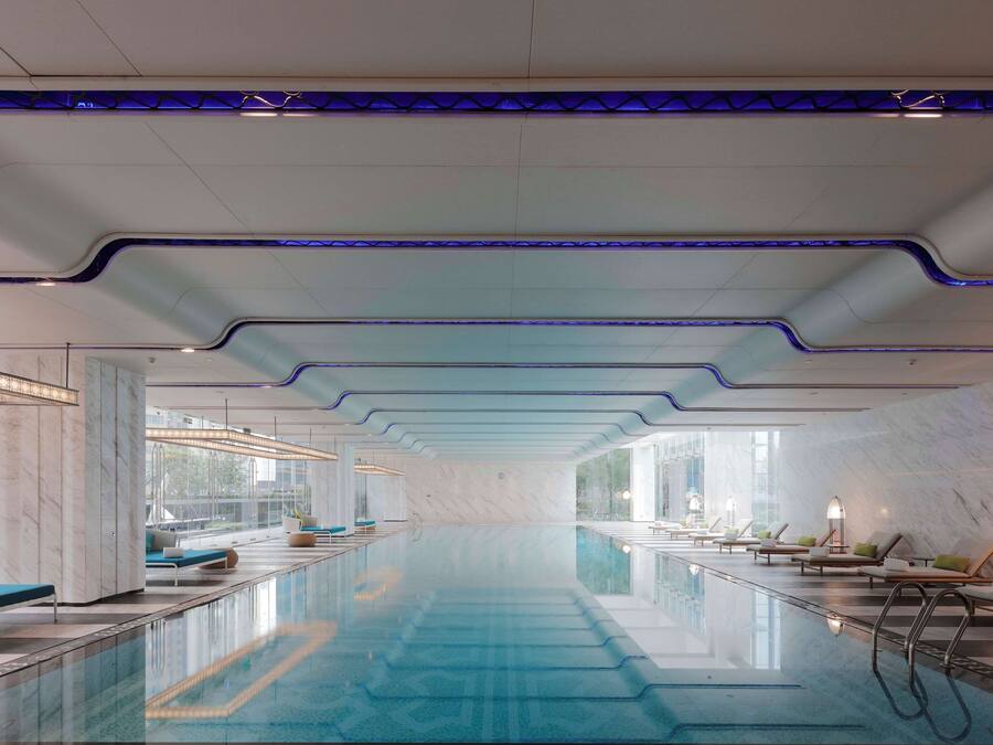 Una piscina interior moderna con una superficie de agua azul cristalina, rodeada de áreas de descanso con asientos y tumbonas.