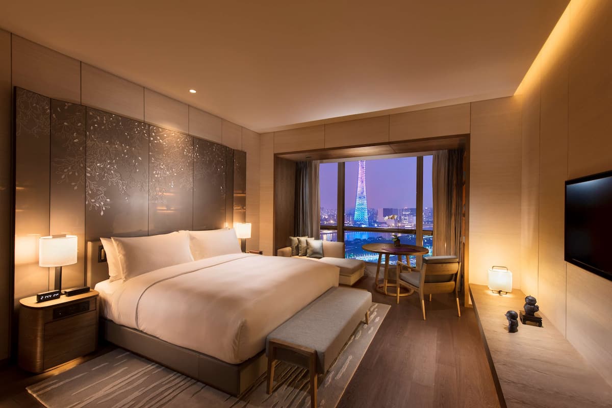 A modern hotel room with a large bed, bedside tables, a desk, and a view of the Eiffel Tower at night.