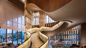 A modern hotel lobby with a curved staircase, large windows, and a seating area.