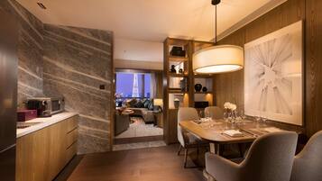 A modern hotel room with a dining area, kitchen, and a view of the cityscape.