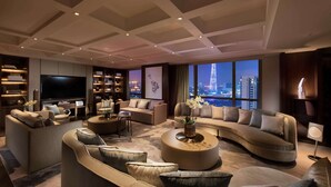 A modern living room with a large flat-screen TV, multiple sofas, a coffee table, and a view of a cityscape at night.