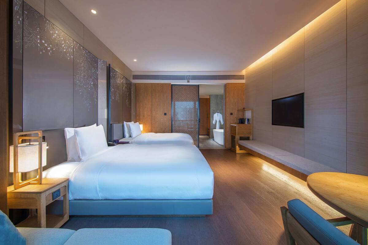 A modern hotel room with a large bed, bedside tables, a TV, and a seating area.
