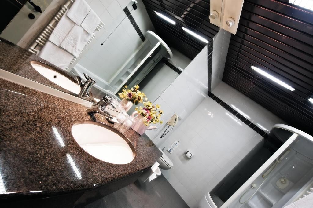A modern bathroom with a granite countertop, two sinks, a mirror, and a shower area.